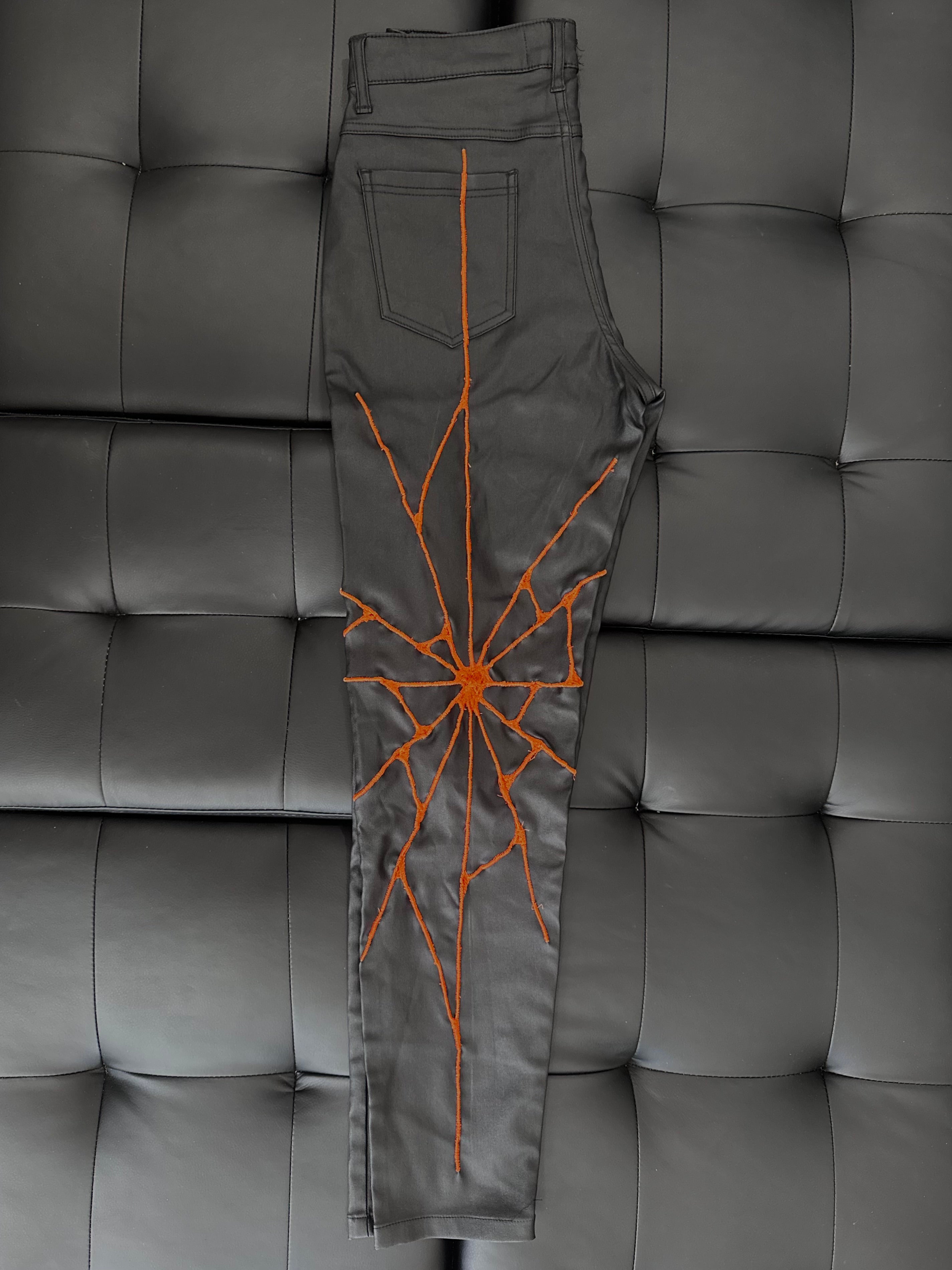 Faux leather pants with a neon orange embroidered web