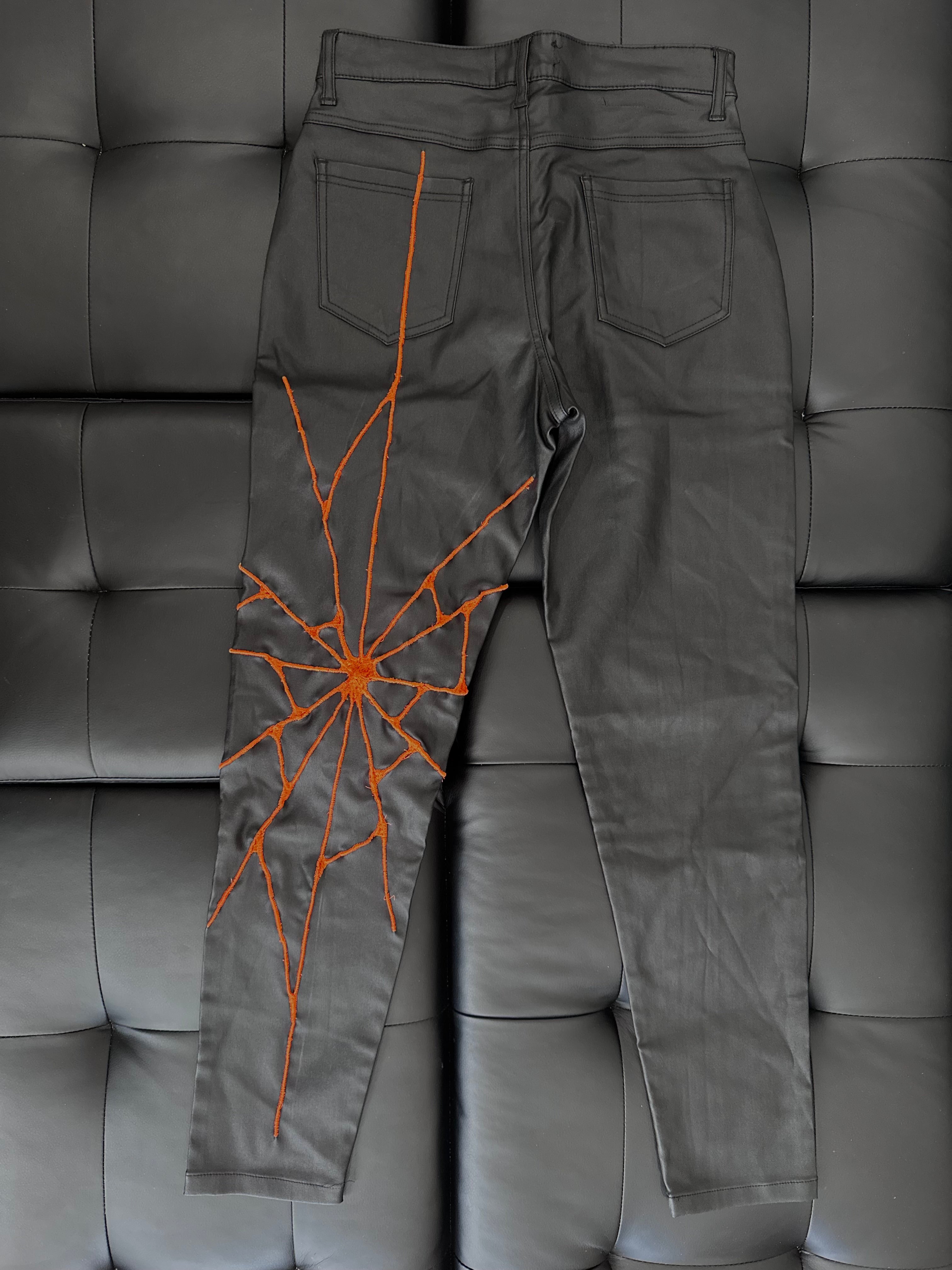 Faux leather pants with a neon orange embroidered web