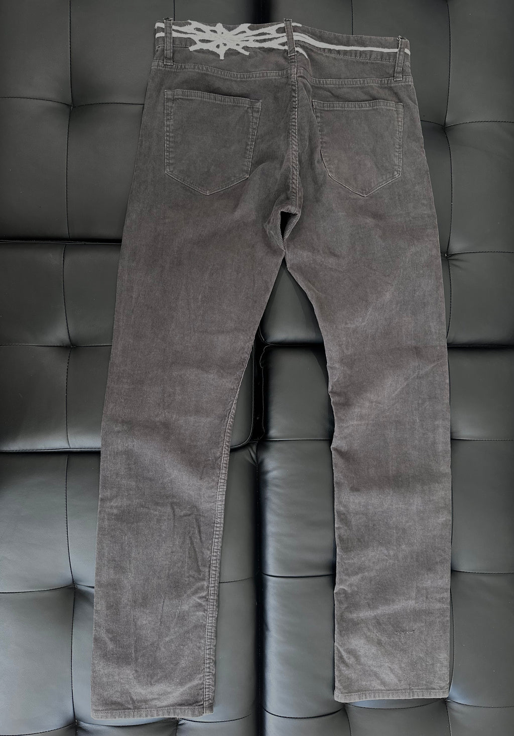 Grey corduroy pants with web embroidered around the waist