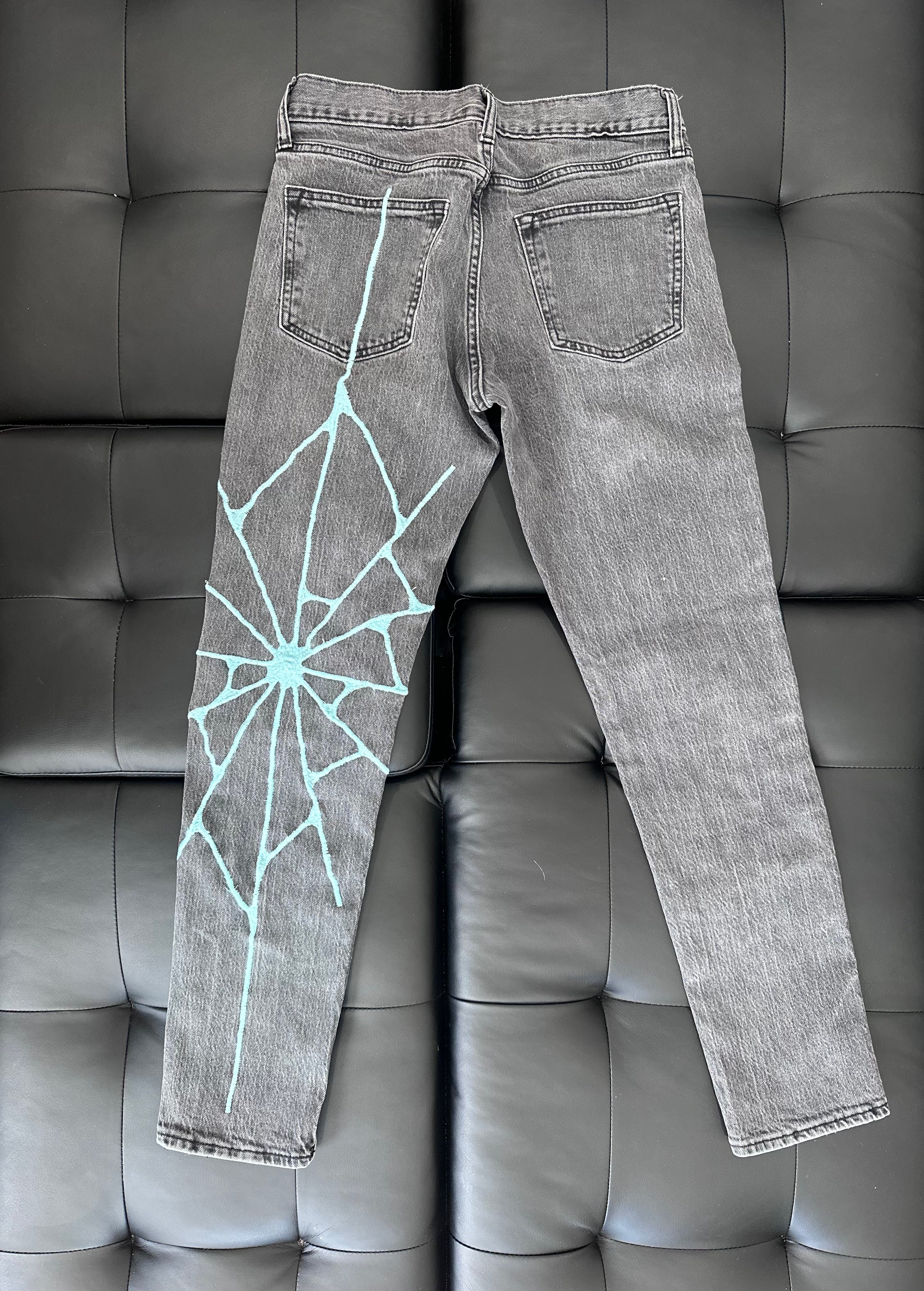 Grey slim taper jeans with a teal embroidered web